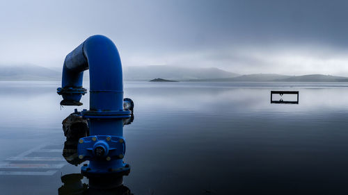 Pipe at lake against cloudy sky