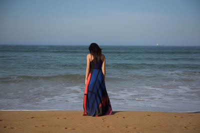 Rear view of woman standing at beach against clear sky