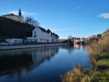 Buildings by river against blue sky