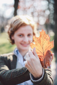 Portrait of smiling young woman showing autumn leaf