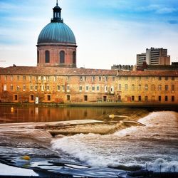 River flowing by historic building against sky