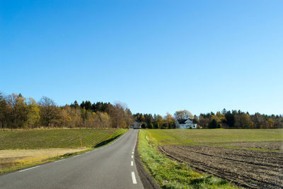 Road amidst field against clear blue sky