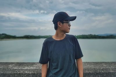 Young man looking away while standing on lake against sky