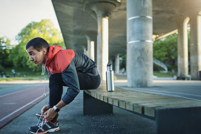 Man tying shoelace while sitting on bench