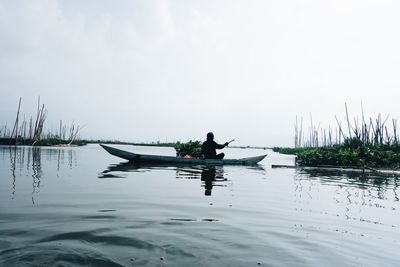 Man sitting on boat in lake against sky