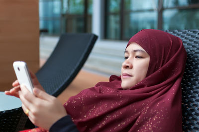 Woman in hijab using mobile phone while relaxing on lounge chair