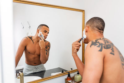 Shirtless man shaving beard in bathroom at home