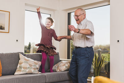 Grandfather and granddaughter jumping and dancing on couch