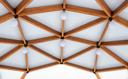 Glass ceiling with lanterns in a brown wooden gazebo outdoors in winter.
