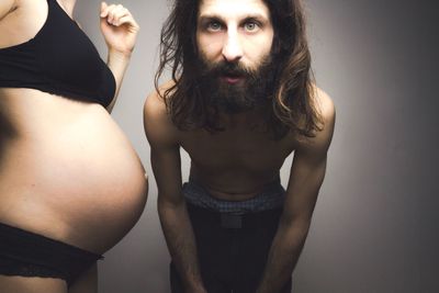 Portrait of man standing by pregnant woman against wall