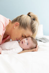 Mother kissing baby girl on bed at home