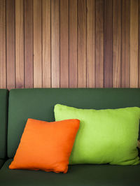 Cushions on empty sofa against wooden wall at home