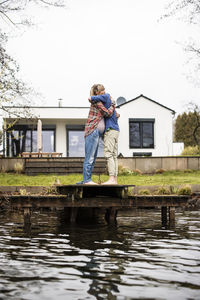 Expectant couple embracing each other standing on jetty in front of house