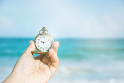 Hand holding clock against sea