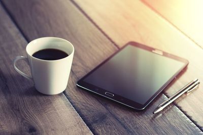 Close-up of coffee cup by digital tablet on table