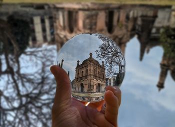 Cropped image of hand holding crystal ball against building