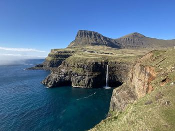 Scenic view of a waterfall sea and mountains against clear blue sky