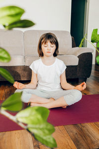 The girl sits in the lotus position and meditates at home in the living room. yoga poses for kids