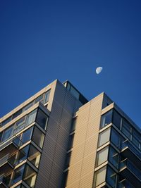 Low angle view of modern building against clear blue sky and moon