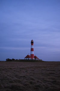 Lighthouse on field by building against sky