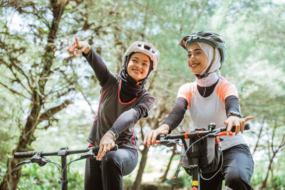 Smiling females with bicycle against trees