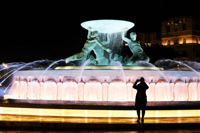 Rear view of man standing by statue at night