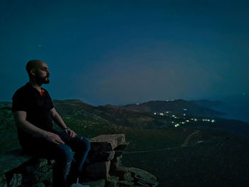 Side view of young man looking at mountains against sky