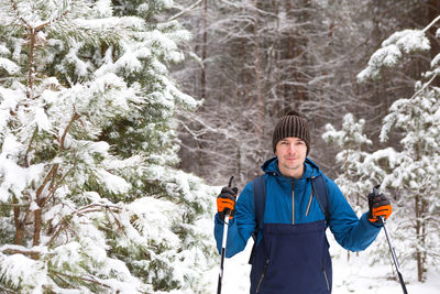 Skier with a backpack and hat with pompom with ski poles in his hands on background of a snowy 