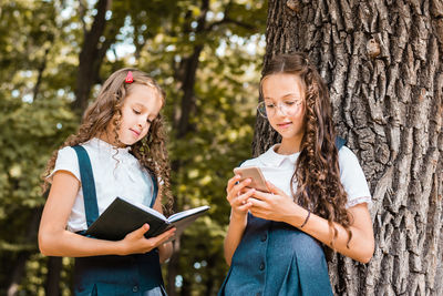 A female student reads a book and a female student looks into a smartphone on a warm day in the park