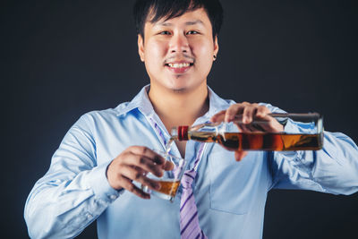 Portrait of smiling man holding drink against black background