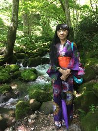 Portrait of woman in traditional clothing standing by stream against plants in forest