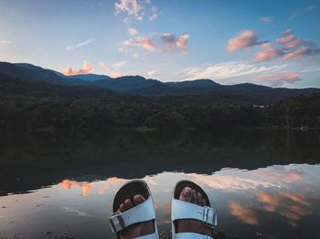 Low section of people on lake by mountains against sky