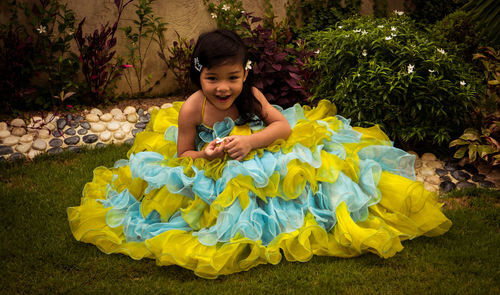 Portrait of cute girl wearing dress while sitting on grassy field