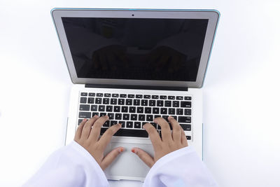 Cropped hands of woman using laptop against white background