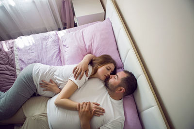 Husband in a white t-shirt with a pregnant wife sitting on the bed at home