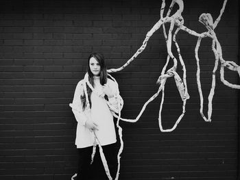 Young woman with ropes standing against brick wall