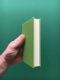 Cropped hand holding diary against green background