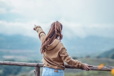 Woman pointing against cloudy sky