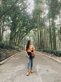 Full length of woman standing on road in forest