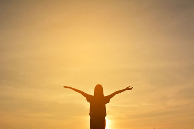 Silhouetted woman with arms outstretched against sky during sunset