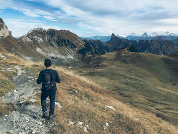 Rear view of man walking on field by mountains