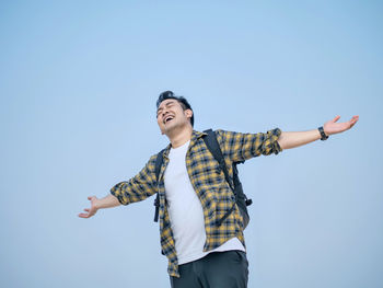Smiling man with arms outstretches standing against clear sky