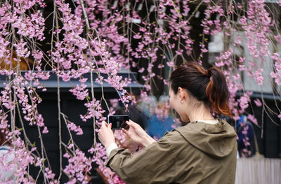 Young woman using phone while standing on tree