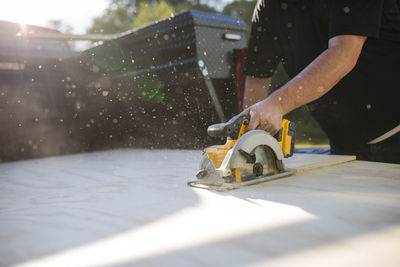 Midsection of man using electric saw while sawing wooden plank in yard