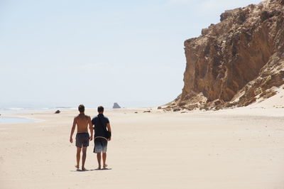 Rear view of men walking on beach against sky