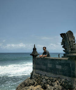 People on rock by sea against sky