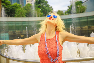 Smiling woman wearing sunglasses while standing by fountain