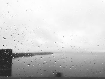 Close-up of wet glass window against sky