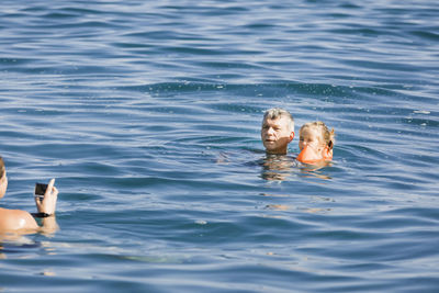 Woman photographing grandfather and granddaughter swimming in sea