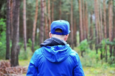 Rear view of man wearing mask on tree trunk in forest